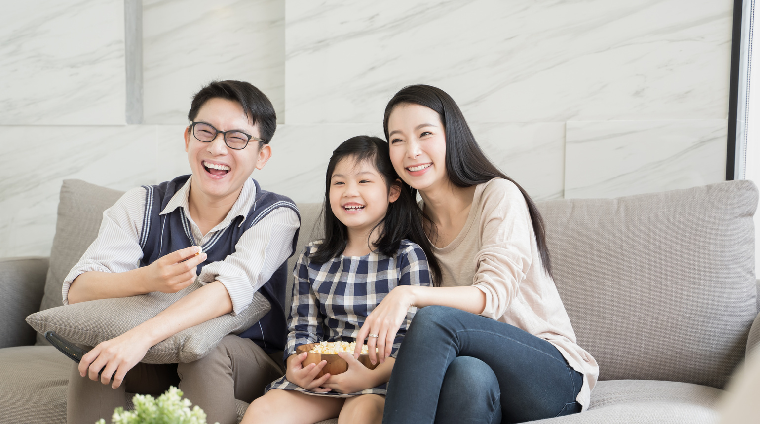 Happy asian family watching tv together on sofa in living room. family and home concept